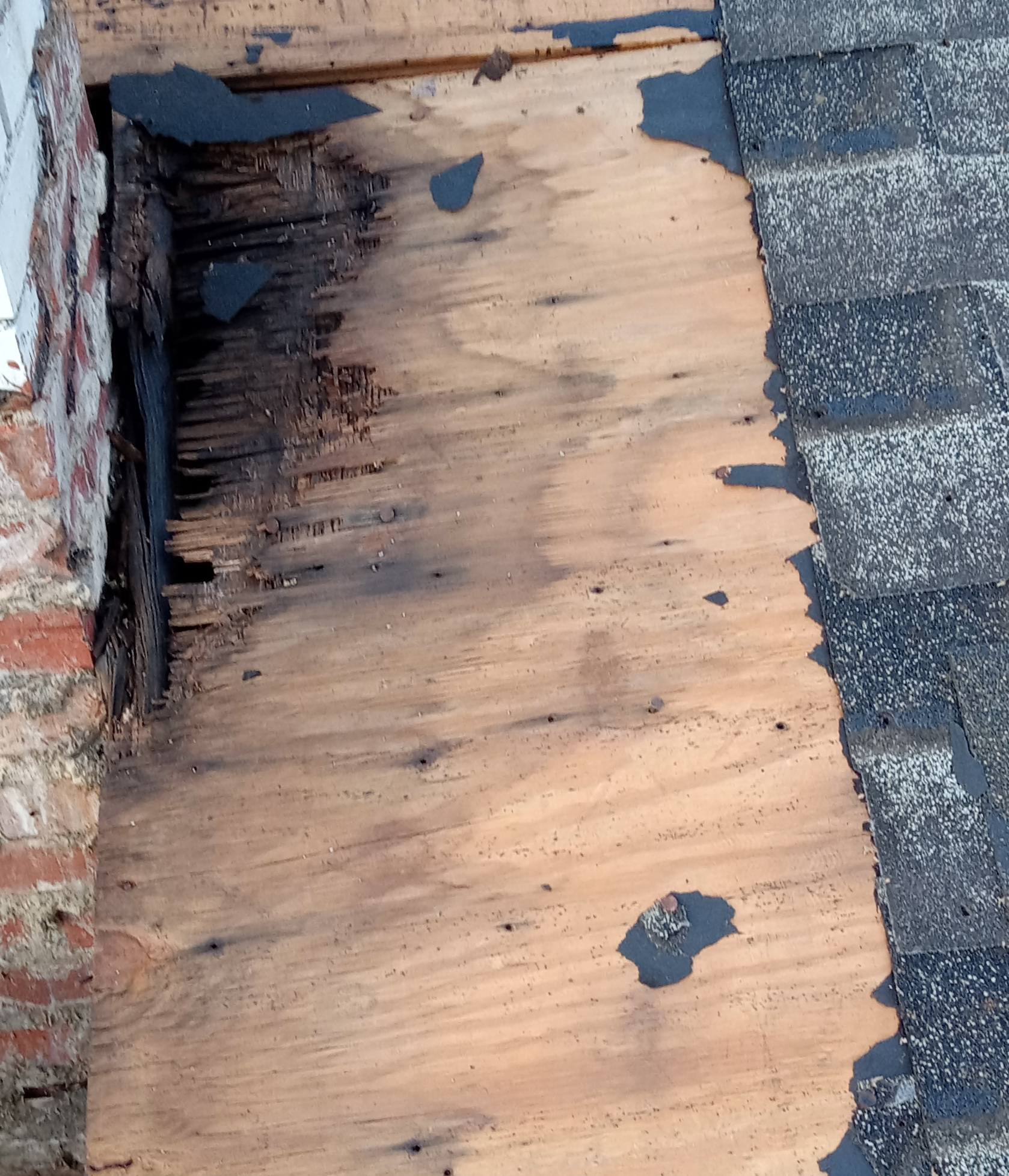 Deteriorated wood roof decking exposed beside a masonry chimney